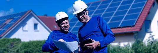 Dois instaladores de painel solar sorrindo enquanto olham para projeto no papel.