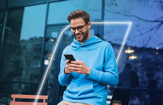 Homem sorrindo, olhando e segurando seu celular com as duas mãos.