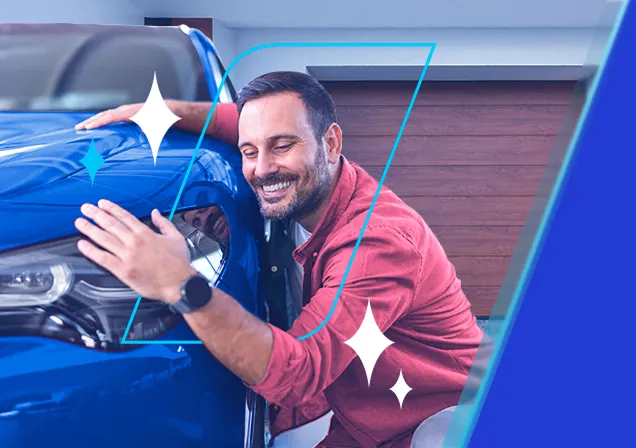 Homem feliz agachado abraçando um automóvel azul em frente uma garagem.