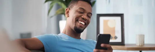 Homem sorridente sentado no sofá olhando o celular