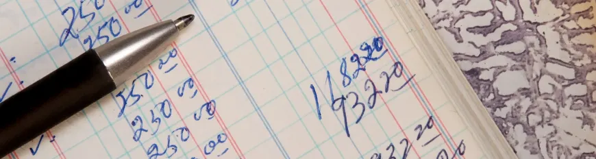 Uma caneta sobre caderno aberto com números anotados a mão.