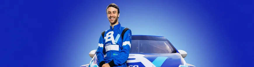 Um piloto sorrindo, com macacão do banco BV. Ele está apoiado em um carro de corrida com fundo azul.