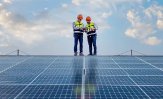 Dois homens com equipamentos de segurança observando anotações em frente a painéis solares.