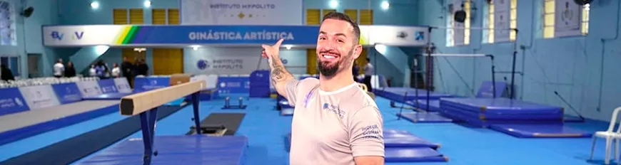 Medalhista Olímpico Diego Hypólito em um centro de treinamento de ginástica artística, apontando para trás.
