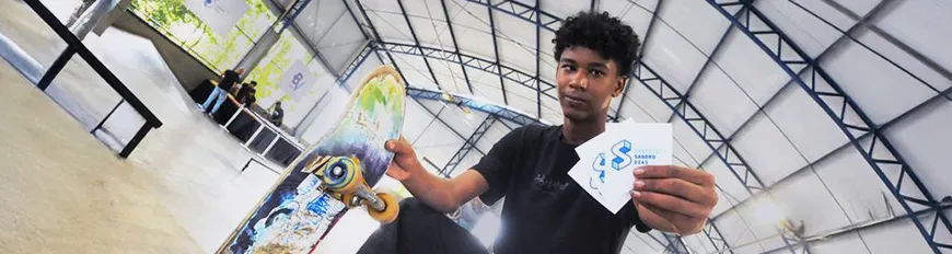 Um jovem segurando um skate em uma mão, e na outra, flyers com a logo do Instituto Sandro Dias.