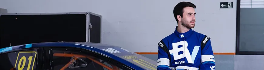 Felipe Baptista, promessa da Stock Car, com roupa de piloto patrocinado pelo banco BV, encostado em um carro.