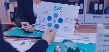 Reunião analisando relatório ESG, com gráfico, documentos e globo em miniatura sobre a mesa.
