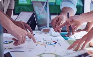 Mãos apontando para um gráfico ESG sobre mesa, discutindo dados e estratégias em ambiente de trabalho.