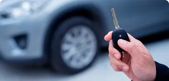 Mão segurando a chave do carro perto do veículo.