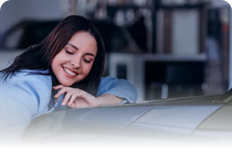 Mulher de olhos fechados sorrindo e apoiada no capô de um carro azul escuro.