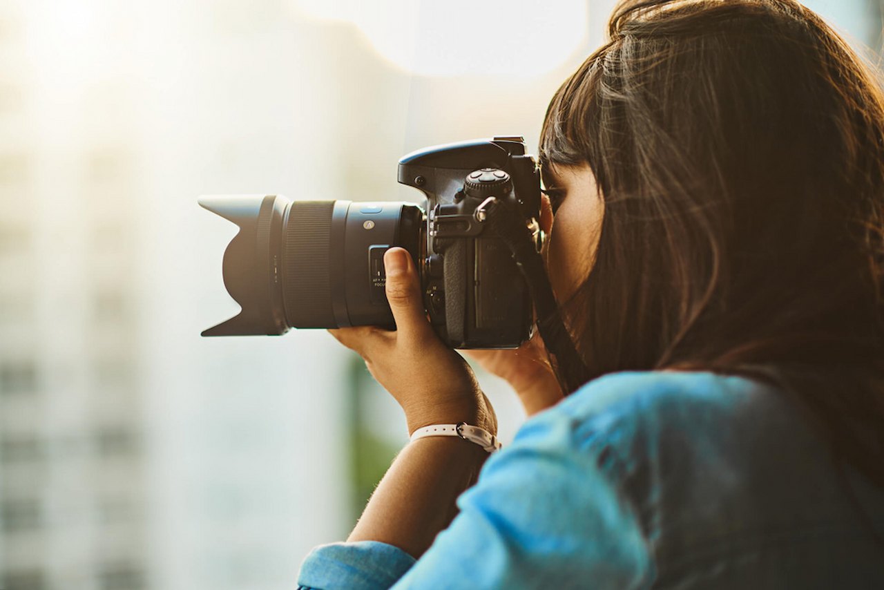 A imagem mostra uma mulher tirando fotos com uma câmera profissional.