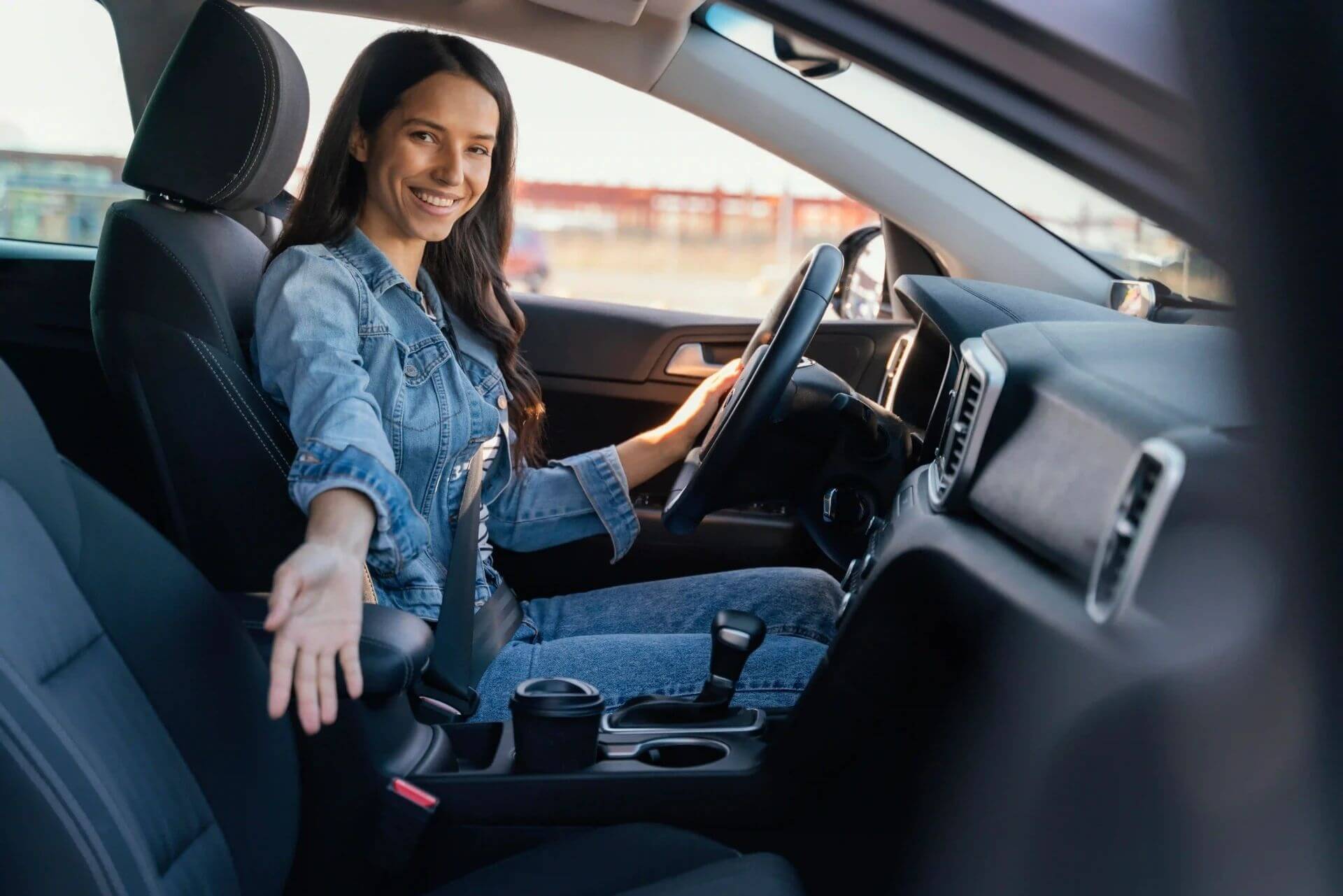 A imagem mostra uma mulher dirigindo seu carro. Ela está sorridente.