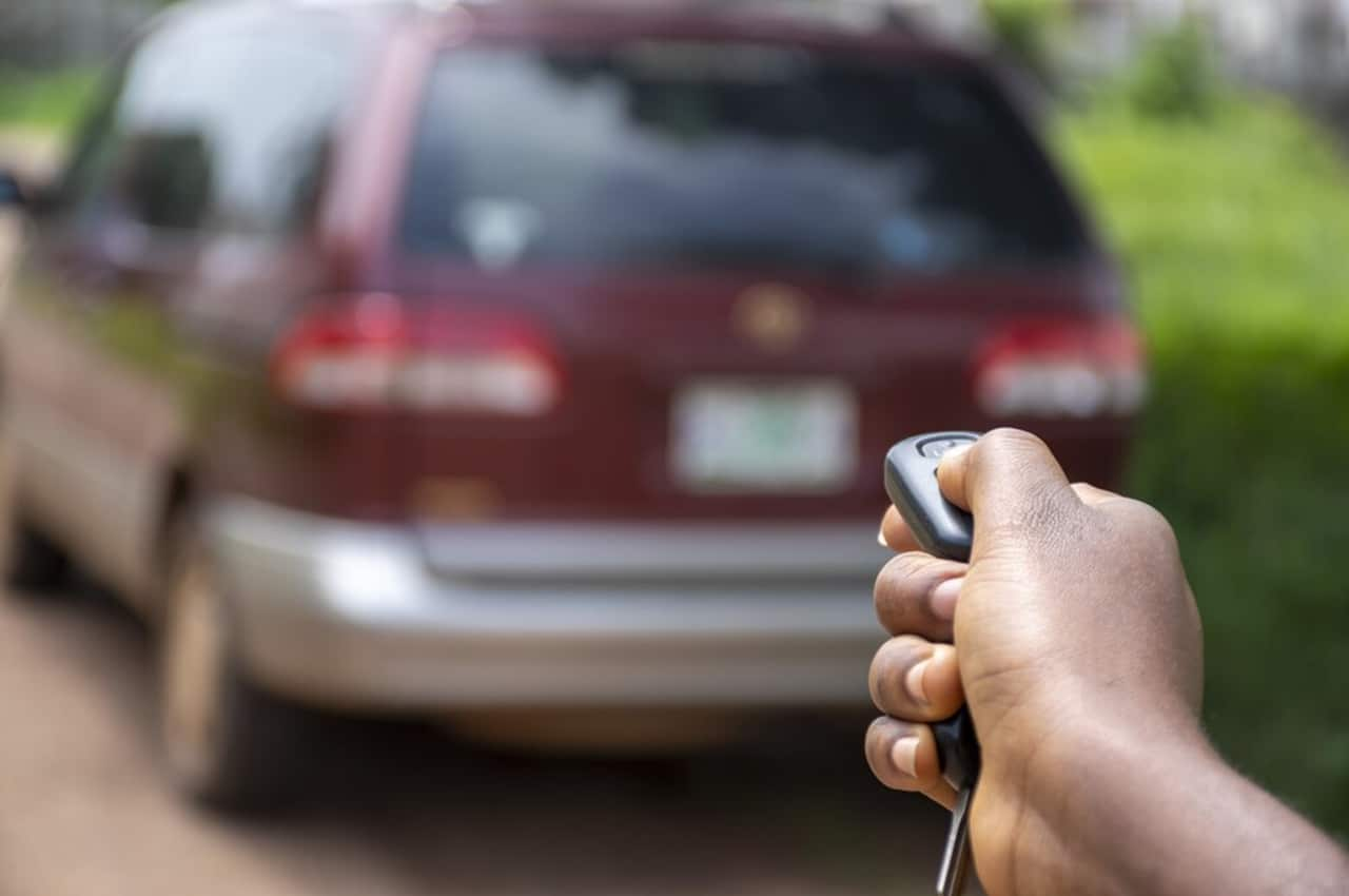 Mão apontando a chave de um veículo para ele, ligando o alarme do carro.