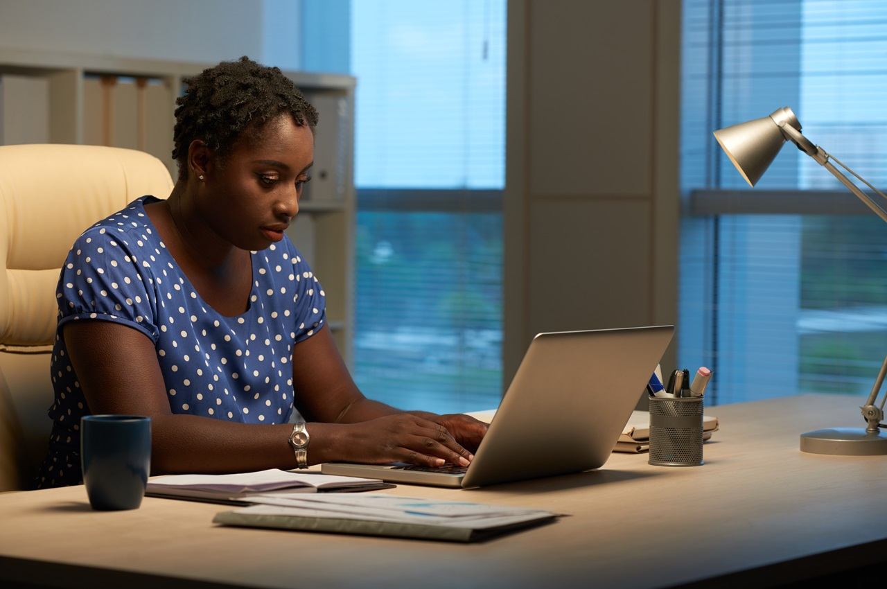 A imagem mostra uma mulher em seu escritório e usando um laptop. 