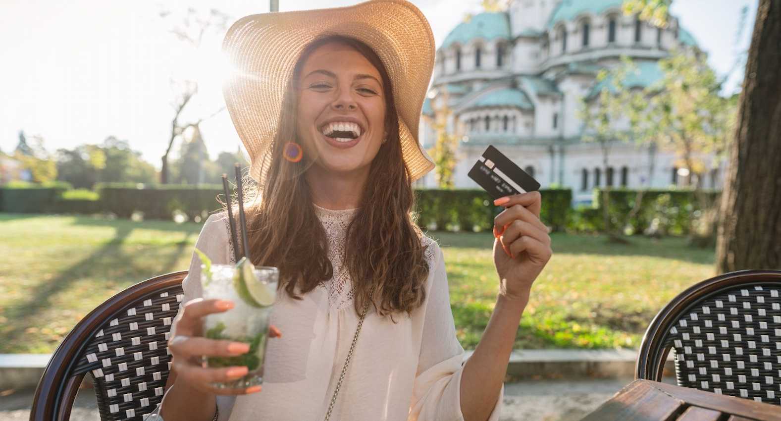 A imagem mostra uma mulher sorridente, tomando uma bebida com limões. Ela está segurando seu cartão de crédito.