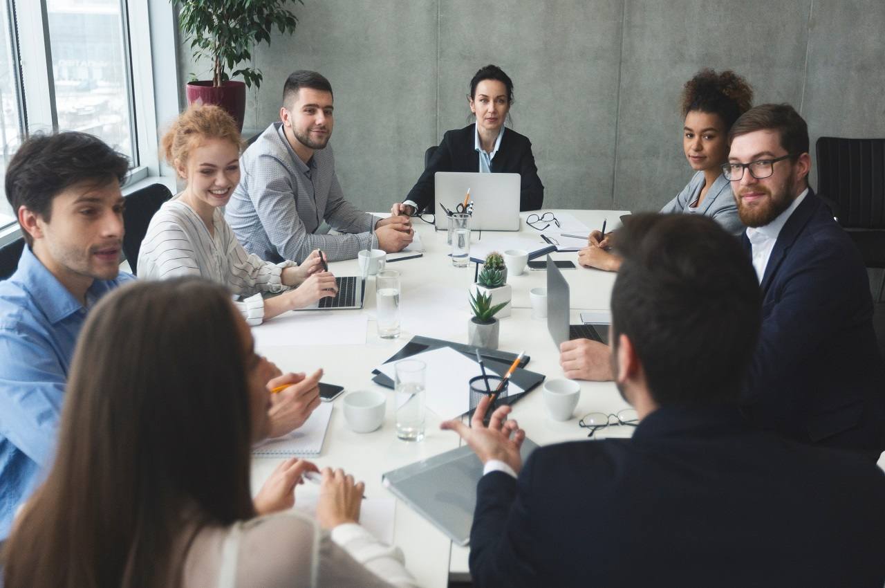 Uma mesa redonda de escritório com funcionários sentados e discutindo sobre energia solar para empresas. 