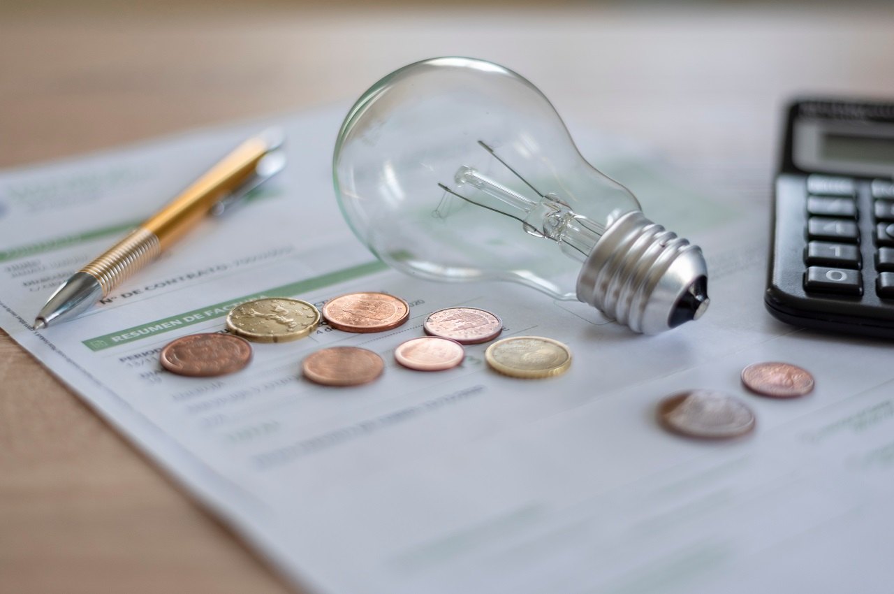 Lâmpada não econômica apagada em cima de um conta de luz e ao lado de moedas e uma calculadora.