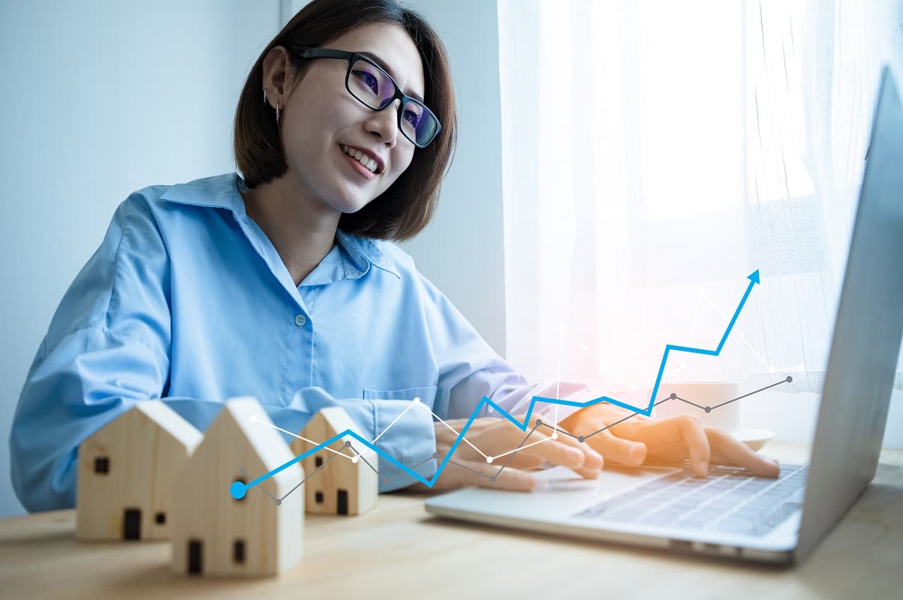 Mulher sorridente de cabelos curtos, usando óculos e pesquisando na internet um gráfico na cor azul sobre Fundos de Investimento Imobiliário.