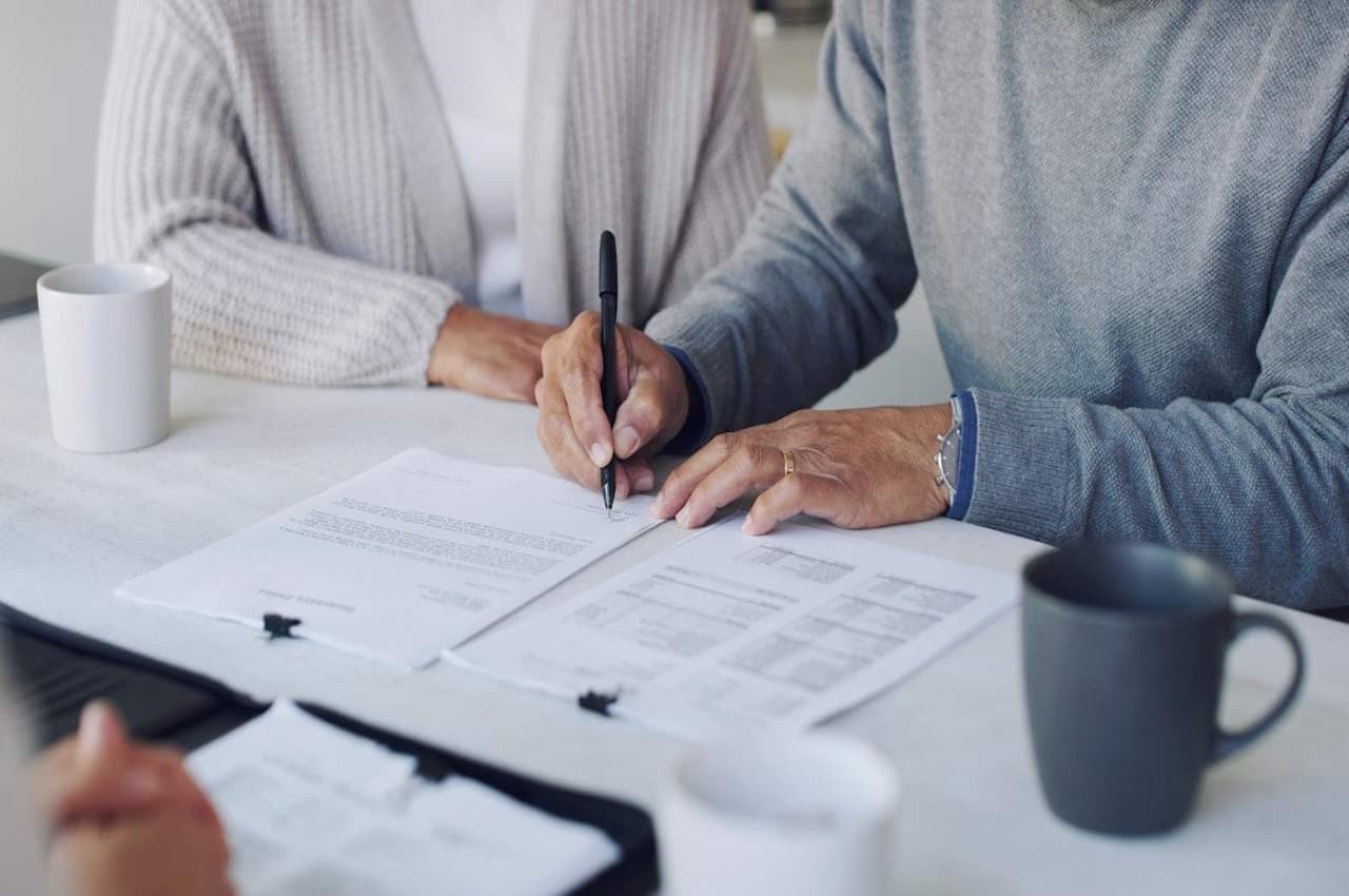 Foco em homem e mulher sêniores assinando um contrato de planejamento sucessório. Os rostos das pessoas não aparecem na imagem.