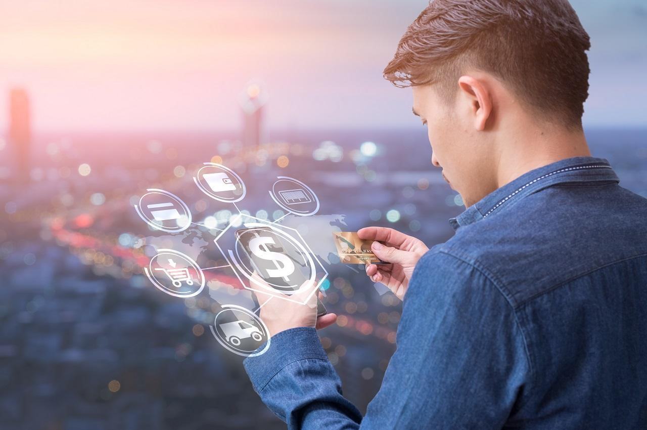 A imagem mostra um homem usando seu cartão de crédito para fazer compras em seu celular. Sob o celular, um ciclo de ícones representando compras.