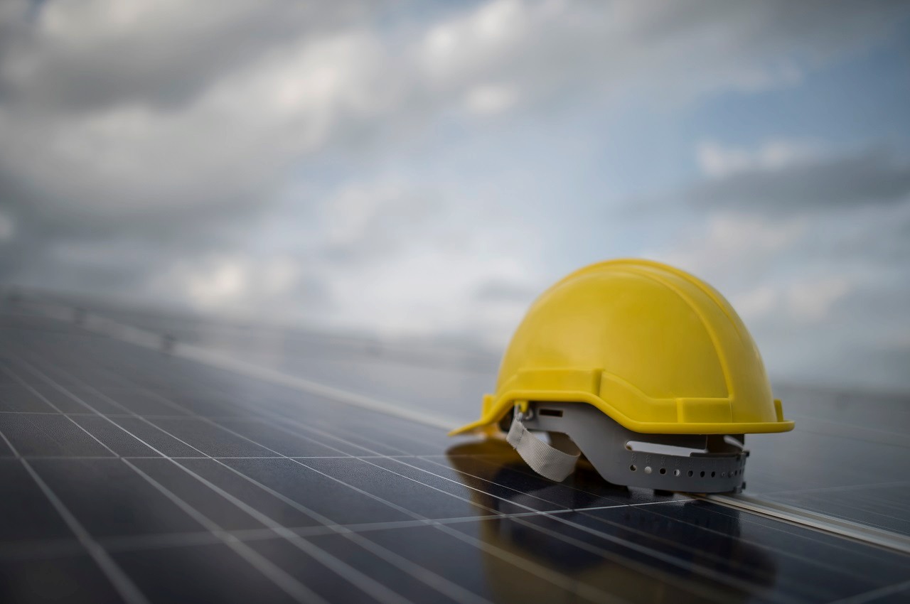 Foco em capacete amarelo de segurança em cima de placas solares e o céu com nuvens de chuva.