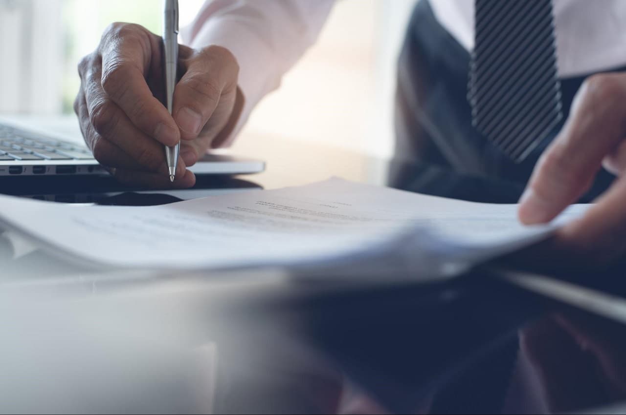 Homem (seu rosto não aparece na imagem) assinando contrato de Power Purchase Agreement em cima de sua mesa.