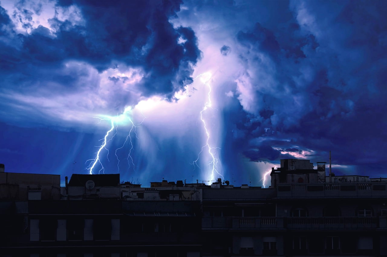 Céu azul com tempo de chuva e raios caindo em região com residências.