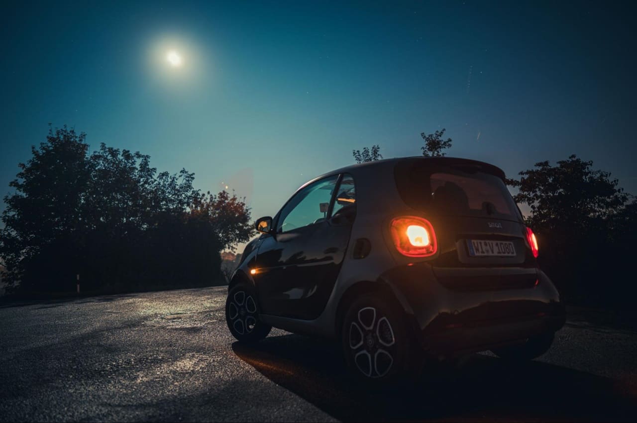 Carro estacionado em estrada de asfalto com as luzes de freio e traseiras acesas. 