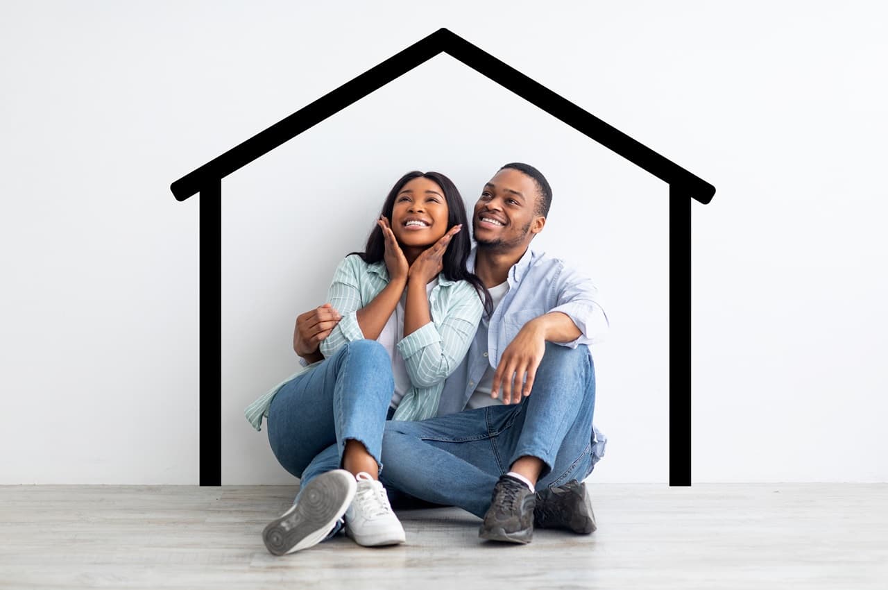 Casal sorridente (homem e mulher) sentados no chão e apoiados em uma parede com a ilustração de uma casa. Eles vestem roupas casuais, tênis, calça jeans e camisas básicas brancas.