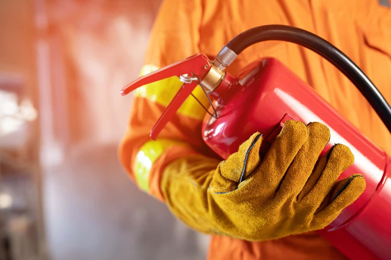 Bombeiro vestindo roupa de segurança contra incêndios e segurando extintor de incêndio.