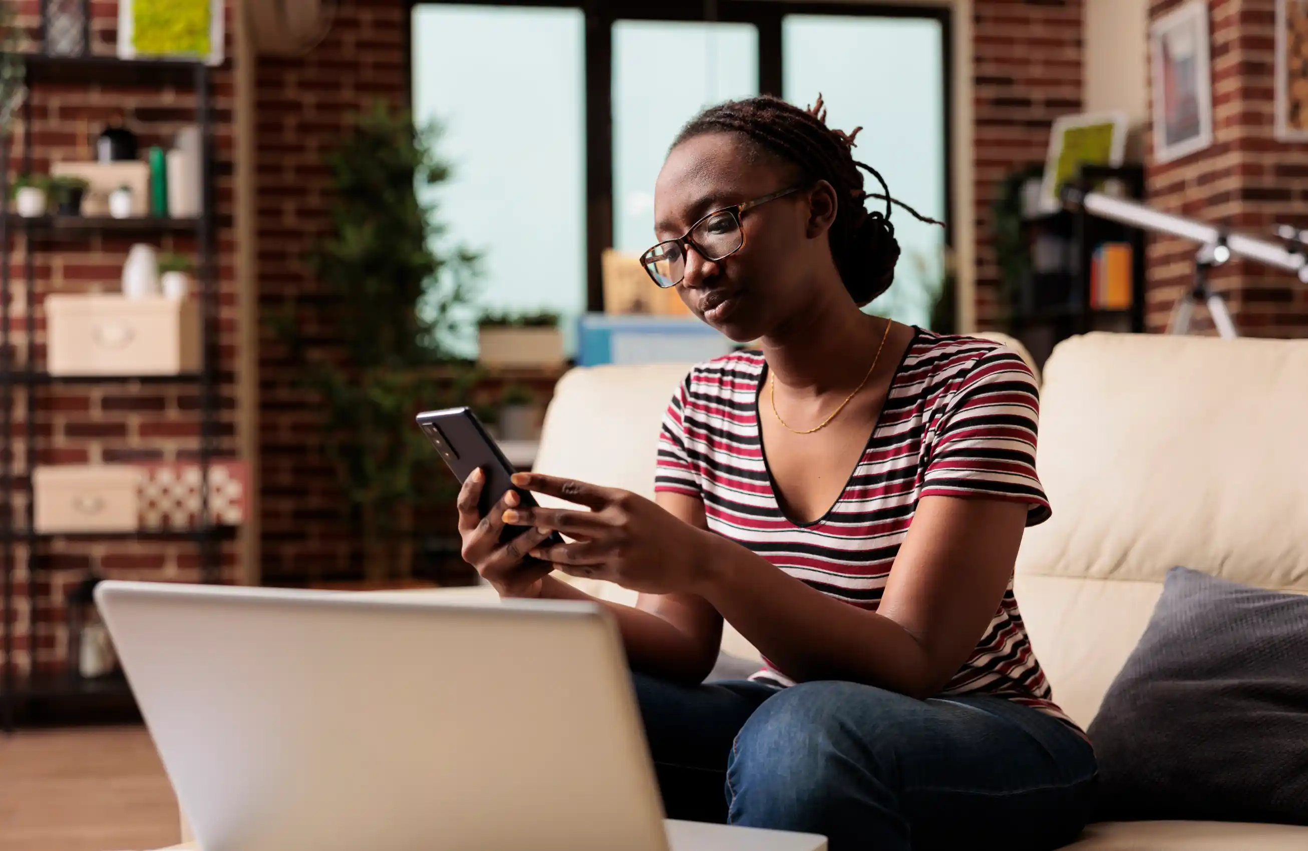 Uma mulher sentada em uma sala de estra enquanto utiliza um smartphone.