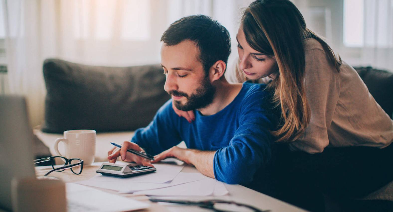 A imagem mostra um casal fazendo contas em uma calculadora.