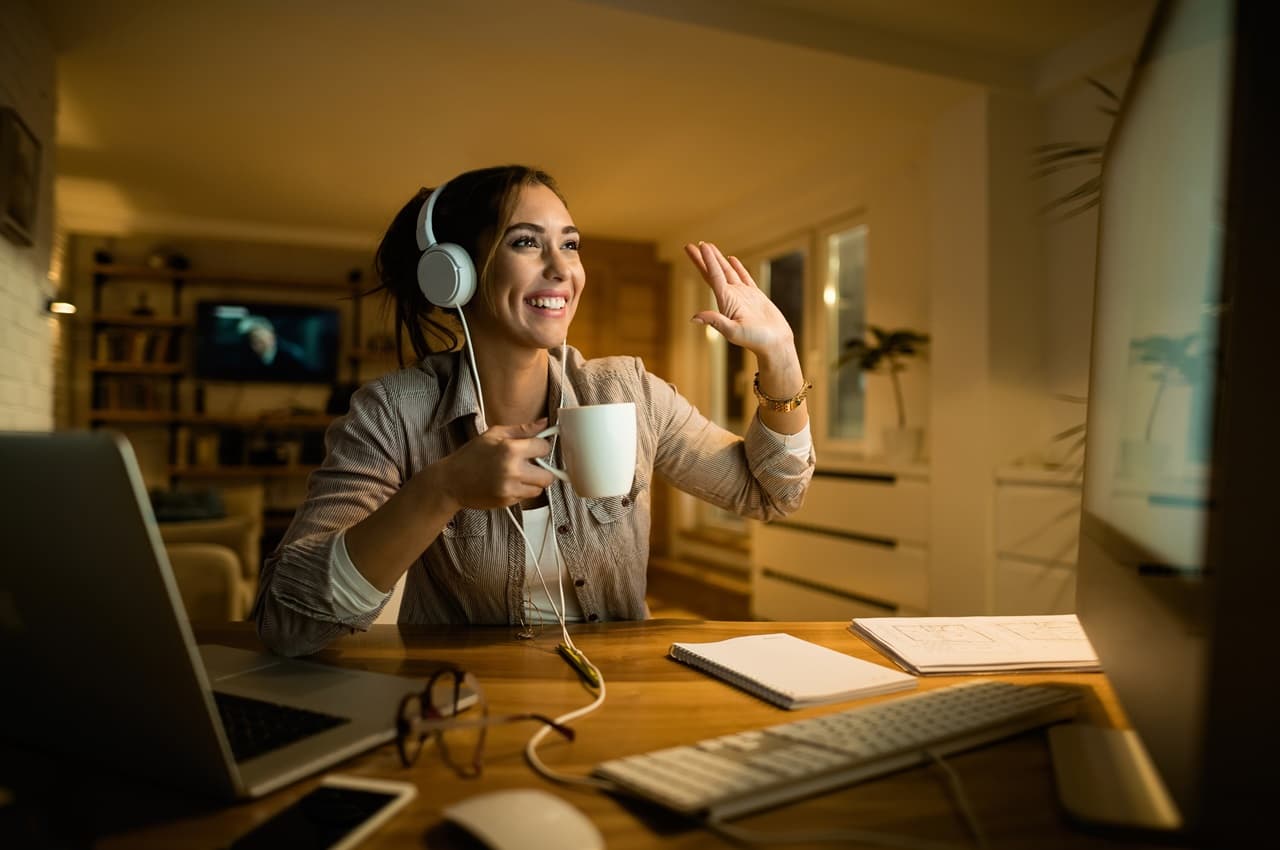 Mulher sorridente, segurando xícara de café, usando fones de ouvido e trabalhando no escritório para ganhar dinheiro no final de semana