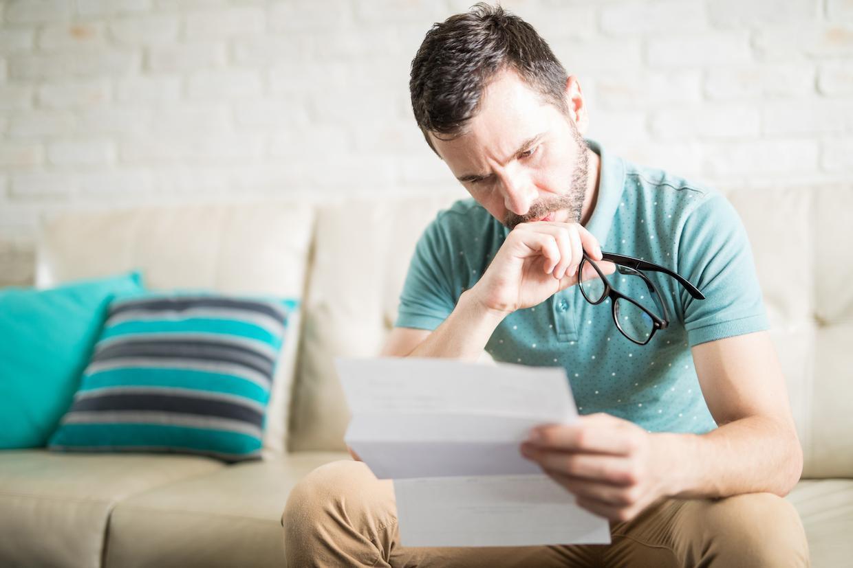 Homem preocupado sentado no sofá, lendo um documento sobre 