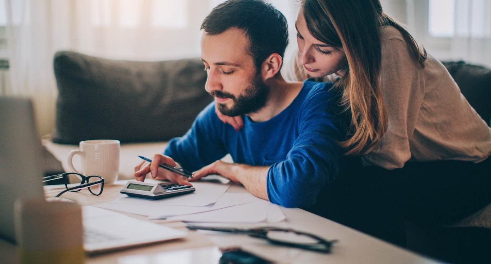 A imagem mostra um casal fazendo um planejamento doméstico e contas em uma calculadora.