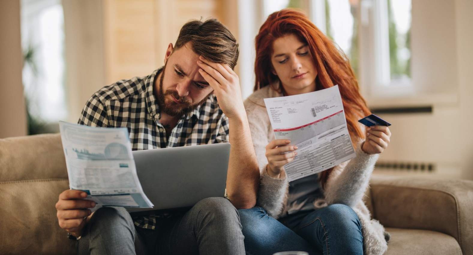 A imagem mostra um casal olhando para seus boletos. Eles aparentam estar preocupados.