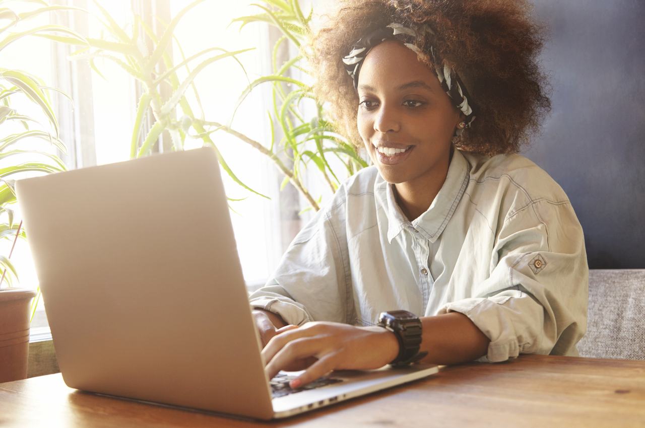 A imagem mostra uma mulher sorridente usando seu laptop.