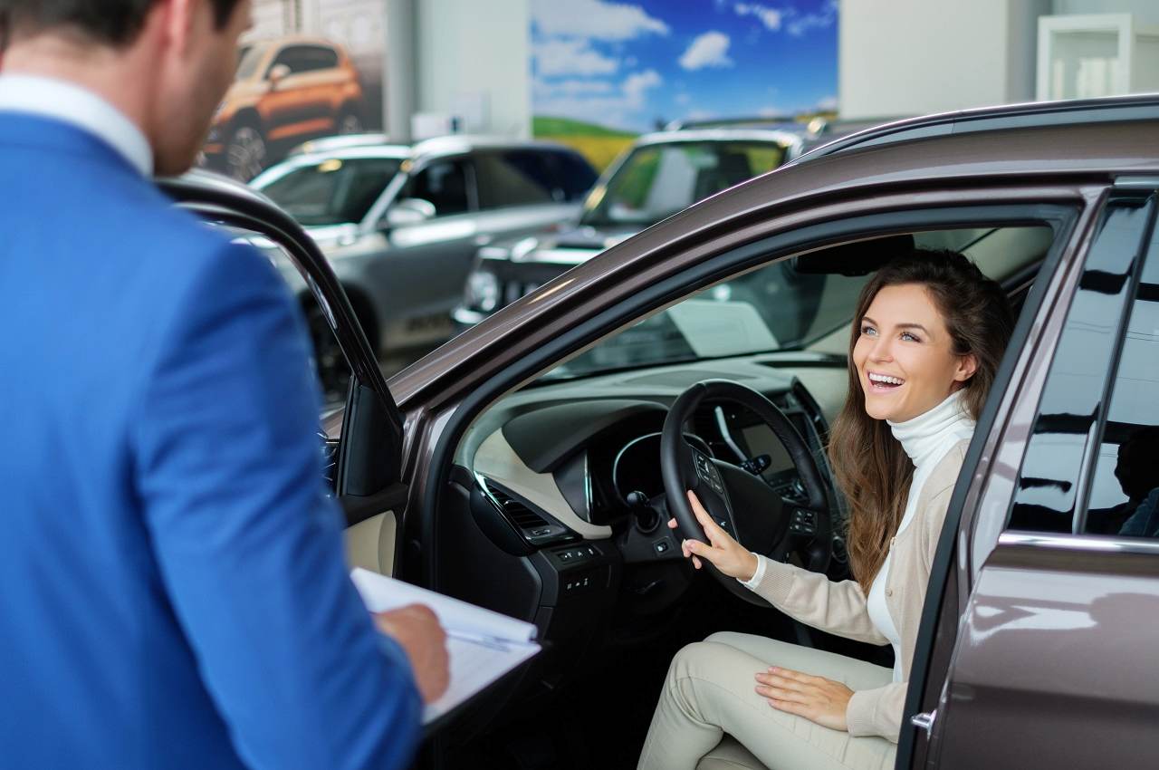 Mulher sorridente sentada no banco de motorista de um veículo à venda e o vendedor sorridente está olhando para ela. 