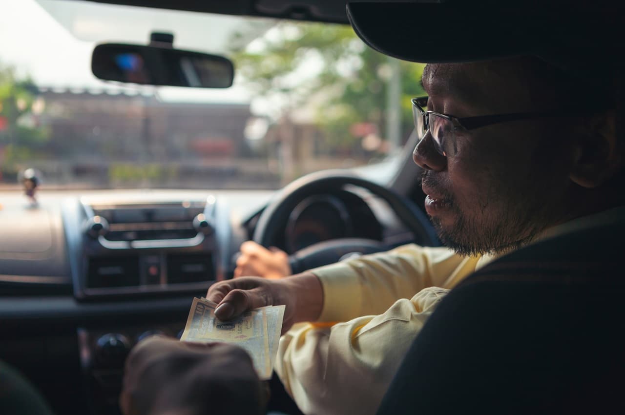 Motorista de aplicativo ganhando direito após realizar a corrida do seu cliente. O taxista veste blusa amarela, boné e tem barba.