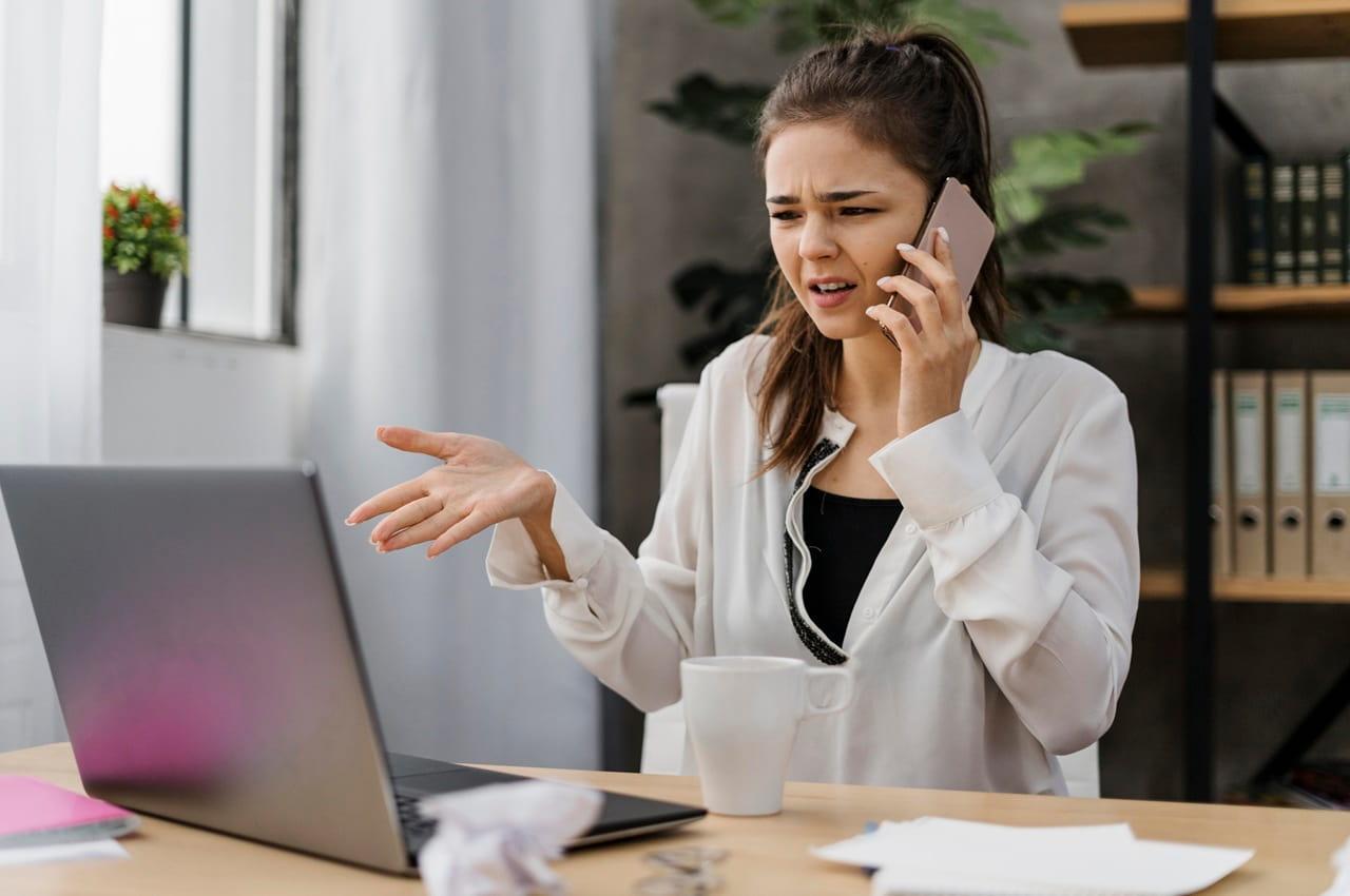 Mulher em um escritório, gesticulando enquanto fala ao telefone. Ela está passando por um golpe do falso financiamento e está com uma expressão de indignação.