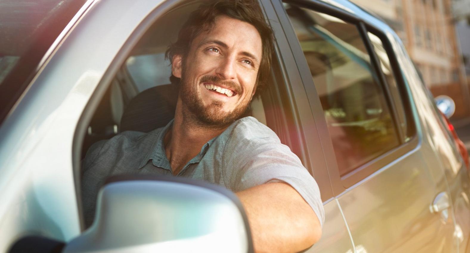 A imagem mostra um rapaz dentro de seu carro, olhando pela janela.