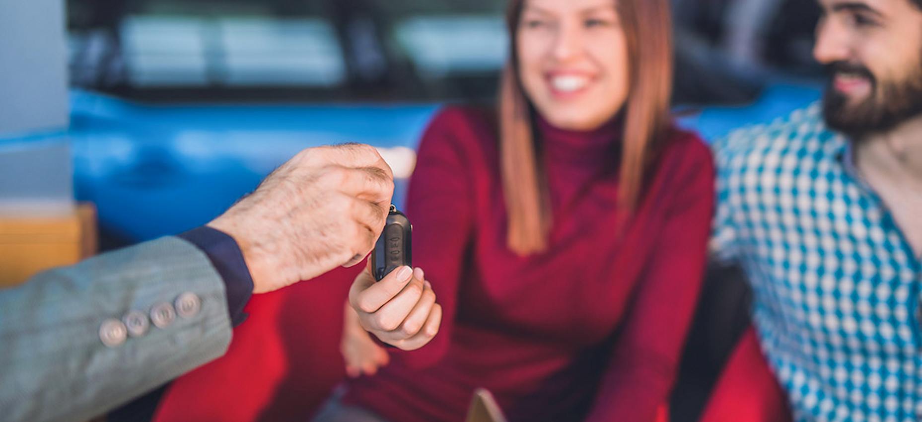 A imagem mostra uma chave de carro sendo entregue para uma mulher.