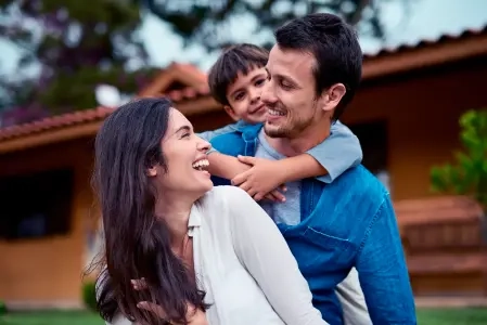 Homem sorridente carrega menino nas costas, ambos olham para a mulher à frente. Retrato de uma feliz família ao ar livre.