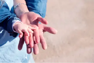 Na imagem há três mãos abertas, sendo de um homem, uma mulher e um bebê. Eles estão vestindo roupas em tons de azul.