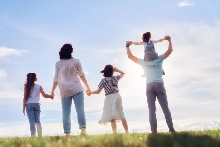 Família de cinco pessoas de mãos dadas, olhando para o céu, em campo gramado, possivelmente parque ou área ao ar livre.