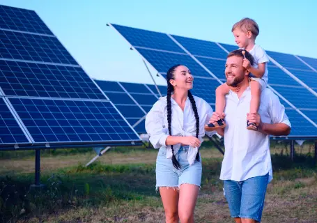 Uma mulher e um homem com uma criança em seus ombros em meio a uma fazenda de placas solares