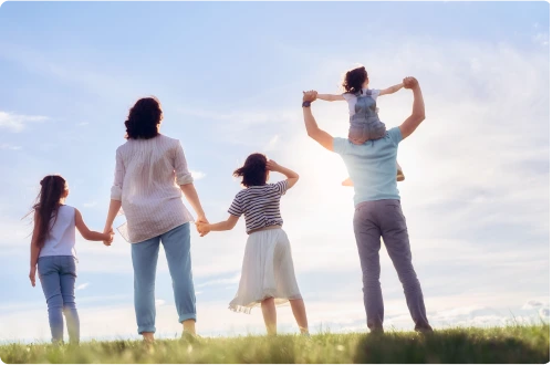 Família de costas em um campo, com uma criança nos ombros do pai e duas segurando a mão da mãe.