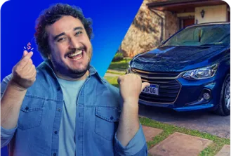 Na imagem, temos um homem branco apontando para um carro azul marinho atrás dele estacionado na garagem de uma casa amarela.