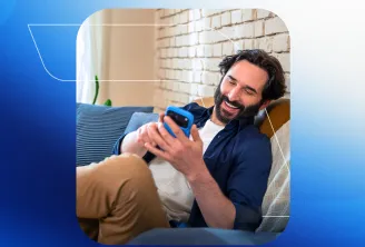Um homem sorri enquanto usa o celular sentado no sofá.