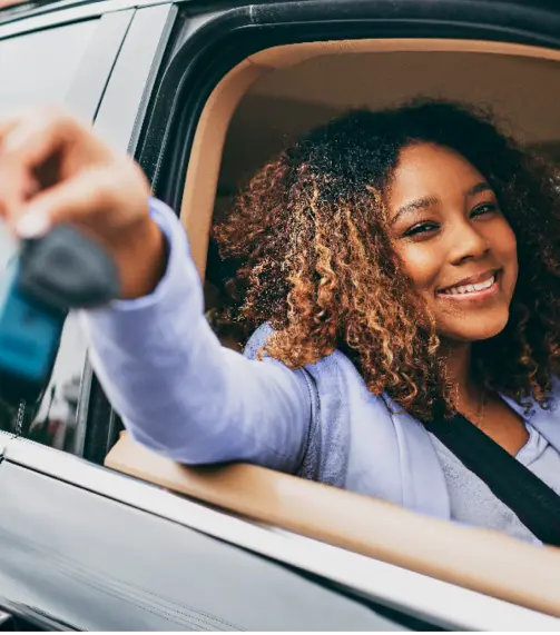 Uma mulher com cabelo cacheado sorri enquanto segura as chaves de um carro pela janela.